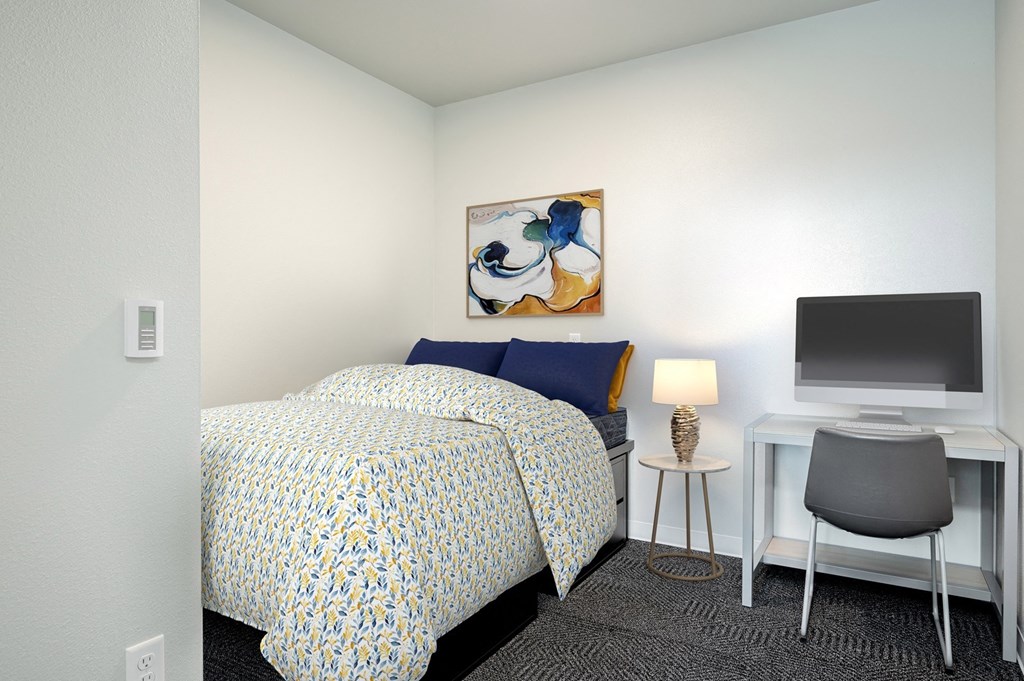 A bedroom with a bed, desk, chair, and painting on the wall.