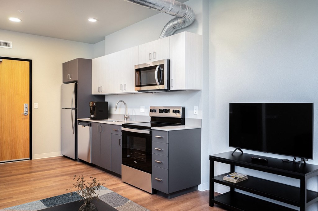 A modern kitchen with a refrigerator, oven, microwave, and a television.
