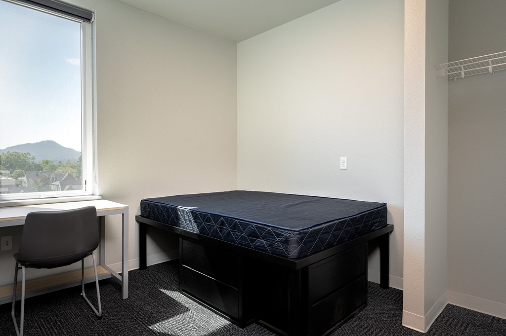 an empty bedroom with a bed and a desk and a window