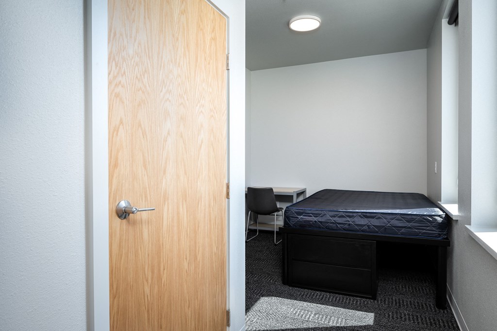 a bedroom with a bed and a door to a room with a desk