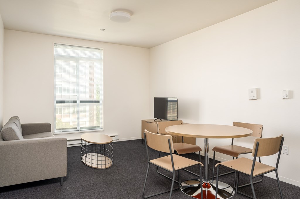 A living room with a grey couch, a round table with four chairs, and a television.