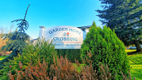 A sign for Garden Home Crossing stands in front of a green hedge.