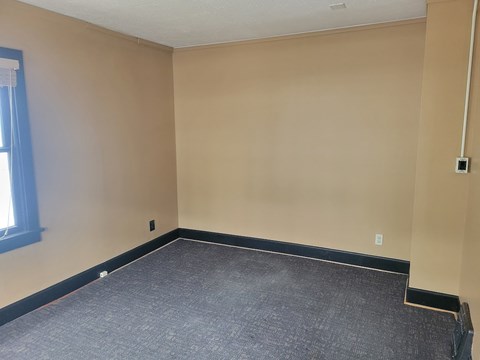 A room with a carpeted floor and a window on the left side.