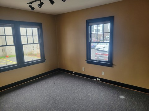 A room with carpeted floor, two windows, and a view of a parking lot.