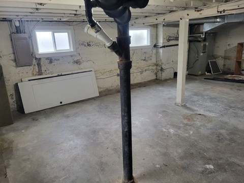 A room with a white cabinet and a window, with a pipe in the foreground.