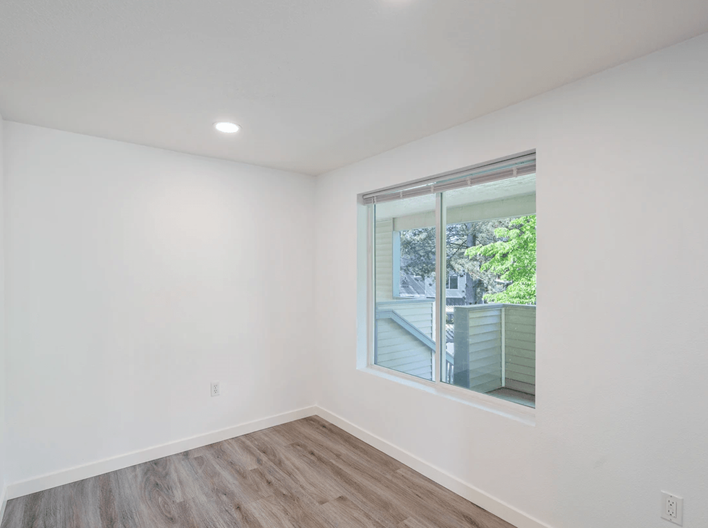 a bedroom with a large window and hardwood floors