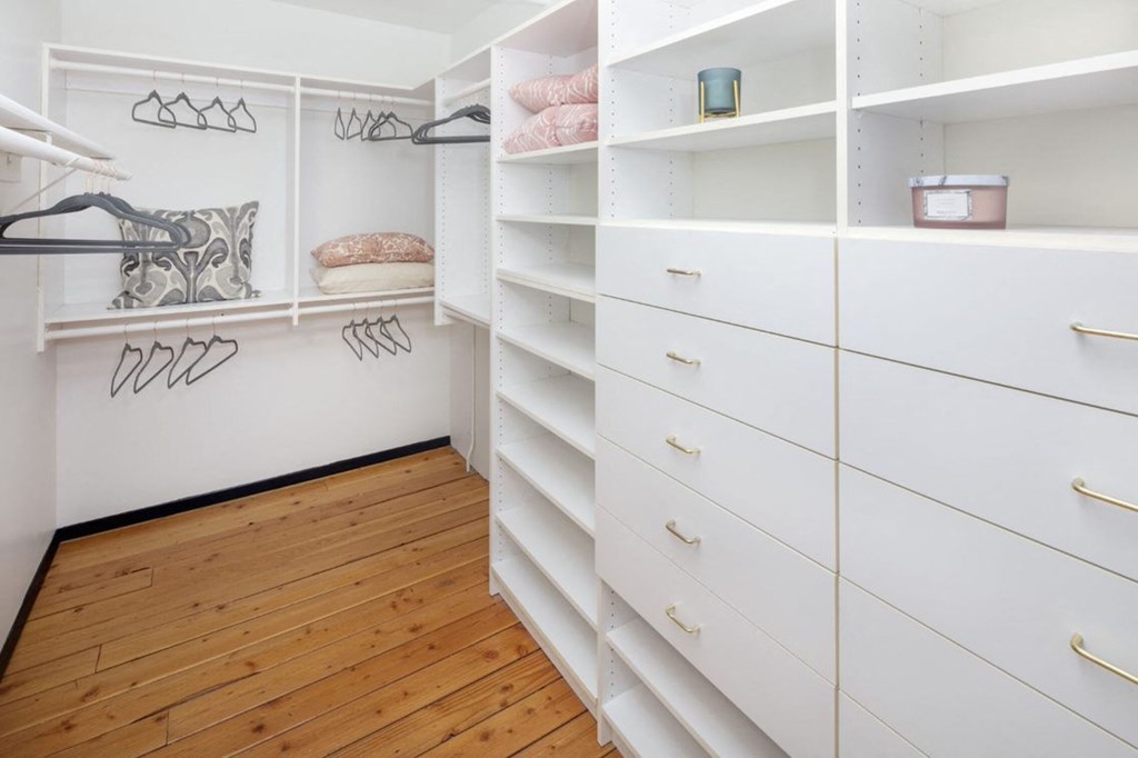 a walk in closet with white shelves and drawers