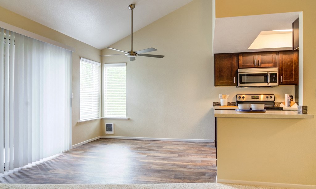 an empty living room with a kitchen and a ceiling fan