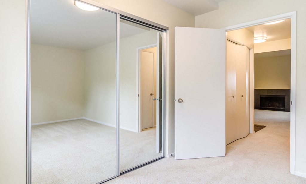 an empty bedroom with mirrored closet doors and a fireplace