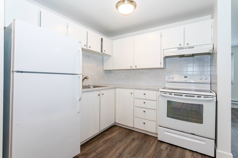 A white kitchen with a refrigerator, oven, and sink.