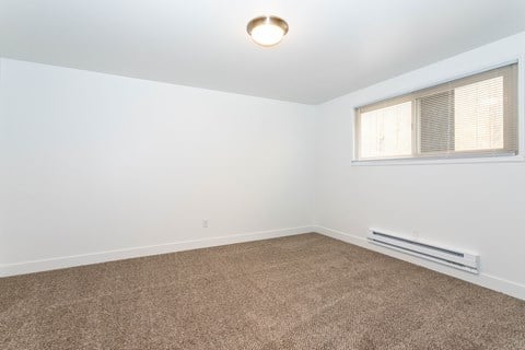 A room with a carpeted floor and a window with blinds.