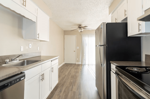 A black refrigerator stands in a kitchen with white cabinets and a sink.