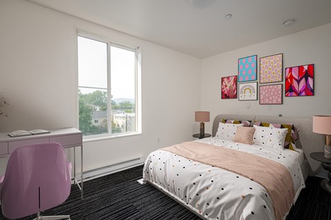 A bedroom with a large bed, a desk with a chair, and a window with a view of the outdoors.