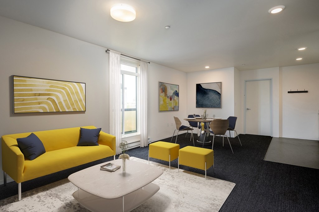 A living room with a yellow couch and a painting on the wall.