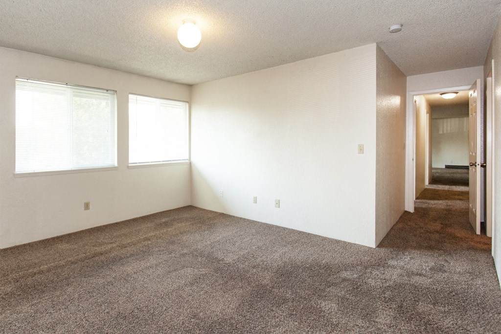 an empty living room with carpet and two windows
