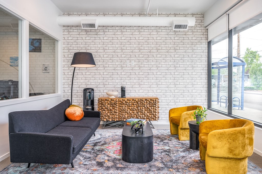 a living room with a black couch yellow chairs and a white brick wall