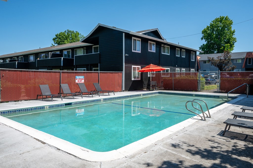 A swimming pool in front of a building with a red umbrella.