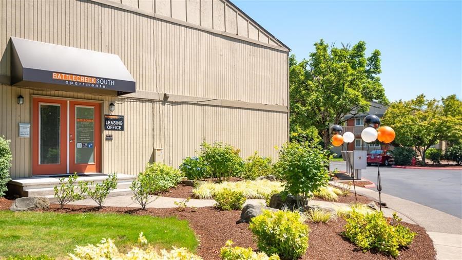 the front of a building with a sidewalk and plants