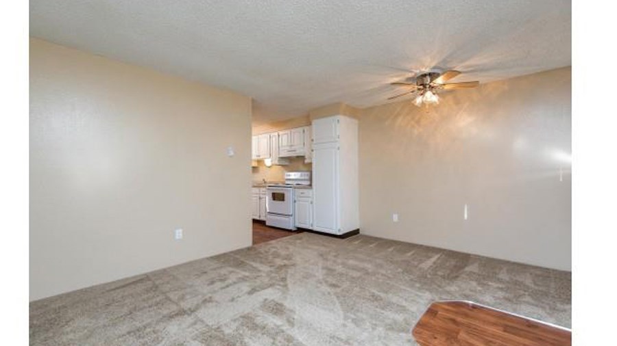 an empty living room and kitchen with a ceiling fan