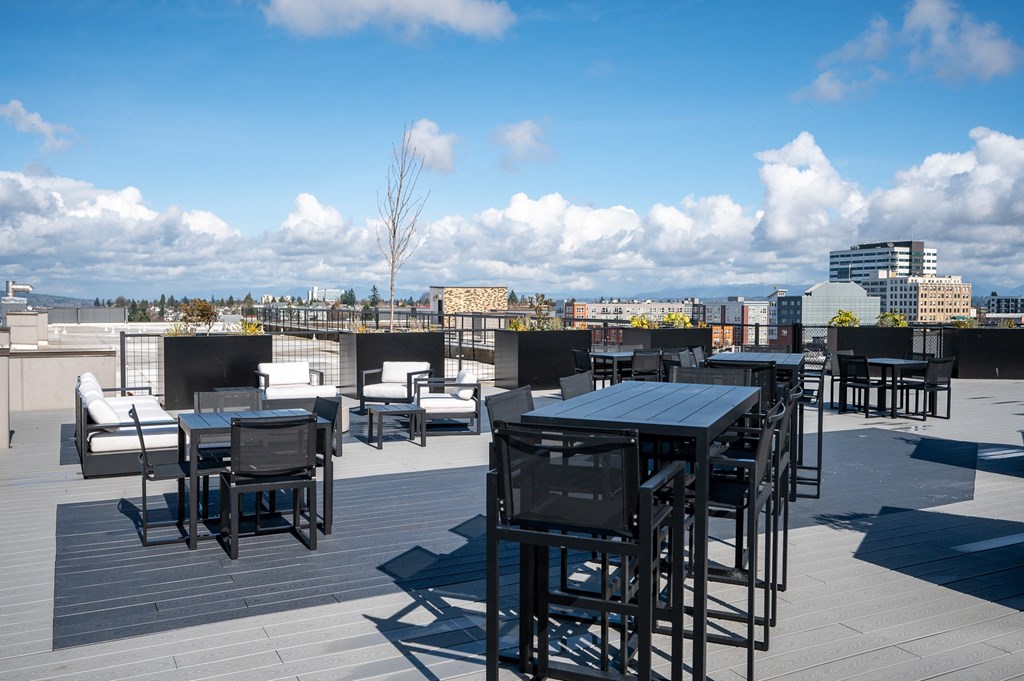 a rooftop patio with tables and chairs and a city in the background
