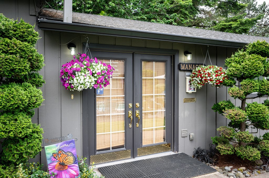 the front of the leasing office with two doors and flowers hanging on the side