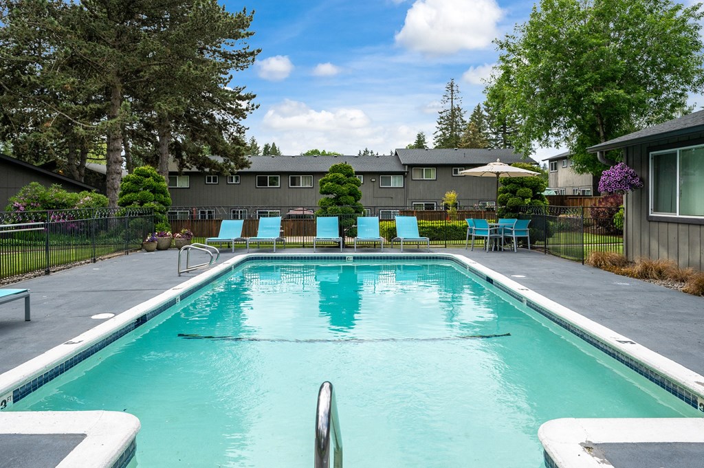 a swimming pool with chairs and a building in the background