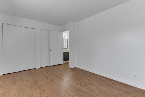 the living room of an apartment with wood flooring and white walls