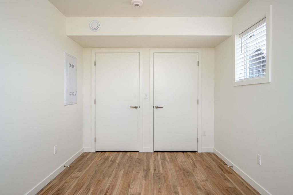A room with two white doors and a window with blinds.