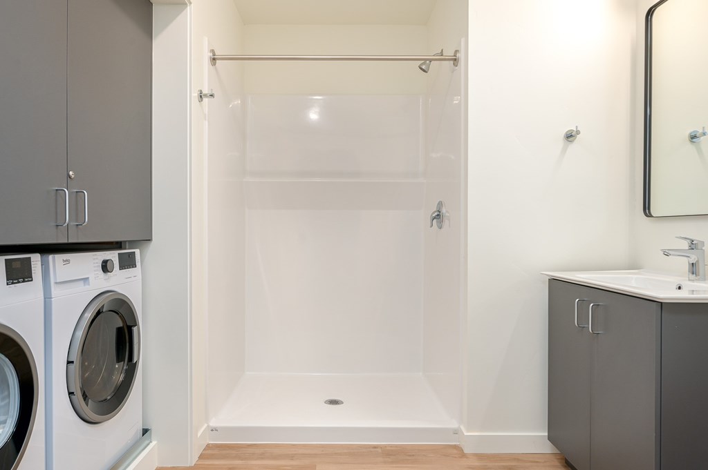 A white bathroom with a walk-in shower and a washer and dryer.