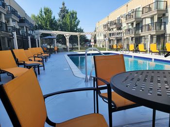 a poolside patio with chairs and tables at an apartment building