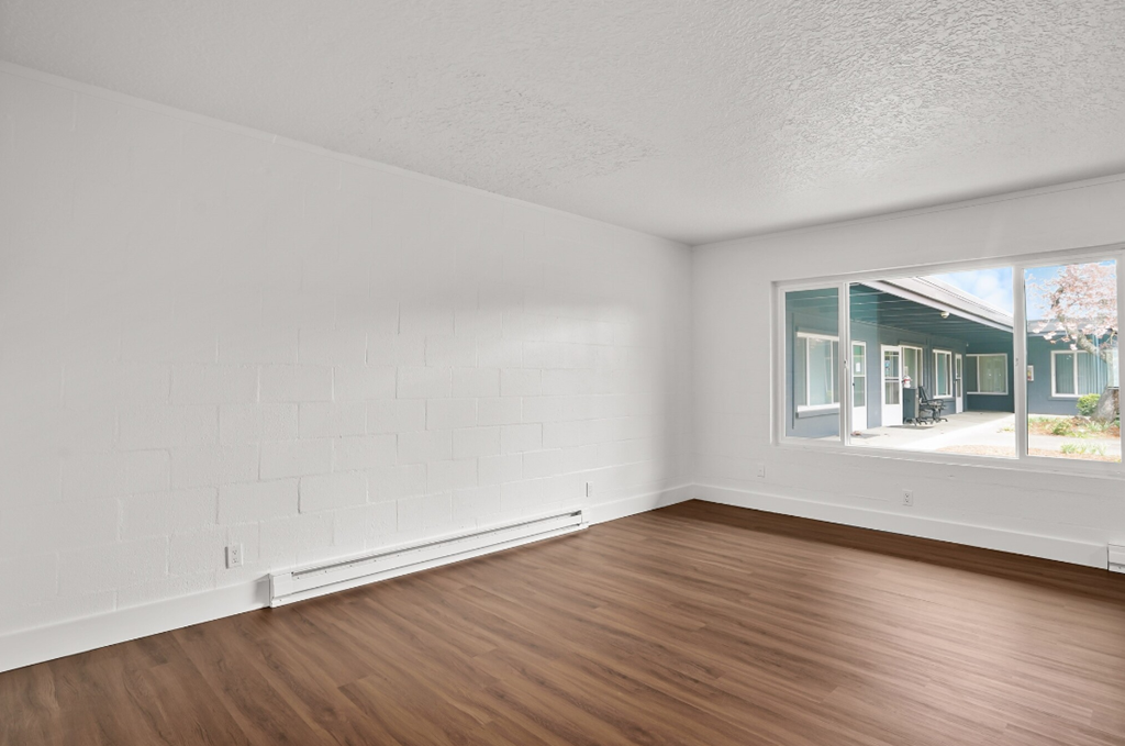 an empty living room with wood floors and a large window