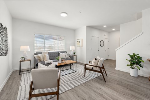 A living room with a grey couch, two wooden chairs, and a striped rug on faux wood flooring.