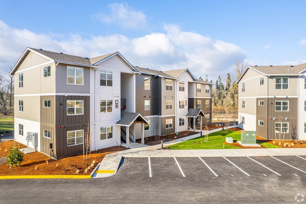 A row of modern apartments with a parking lot in front.