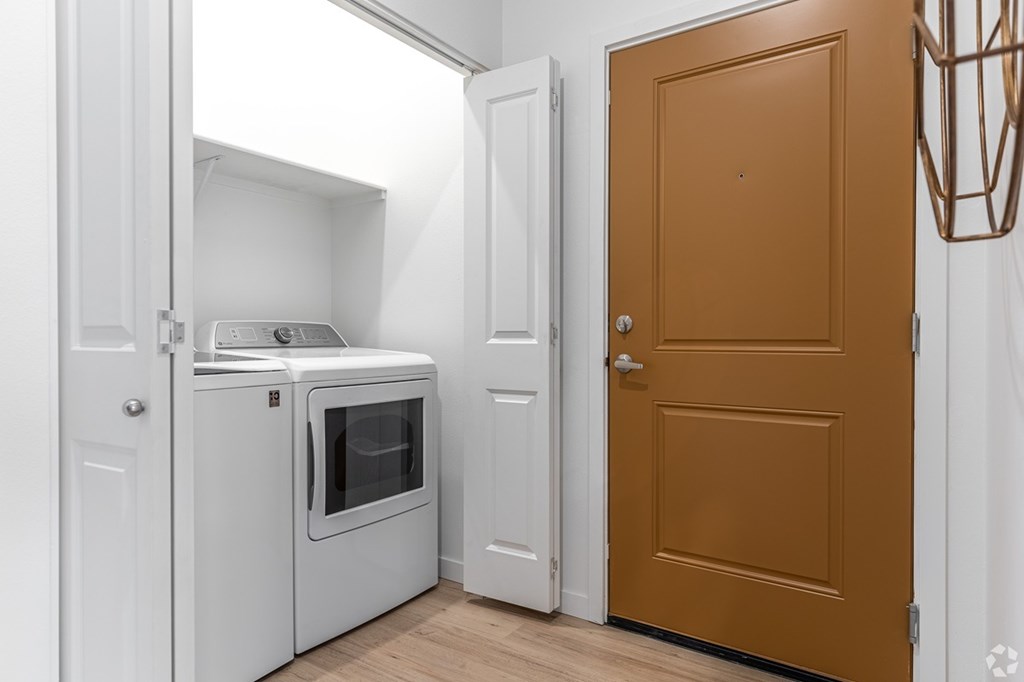A brown door is in a white room with a white oven.