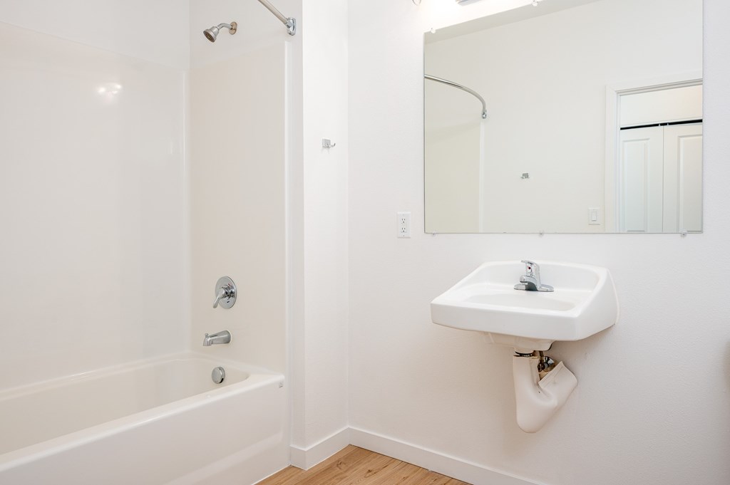 A white bathroom with a sink, mirror, and bathtub.