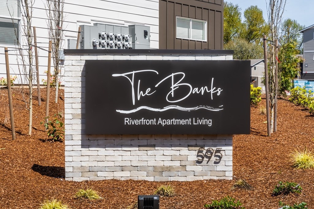 A sign for The Banks Riverfront Apartment Living stands in front of a building.