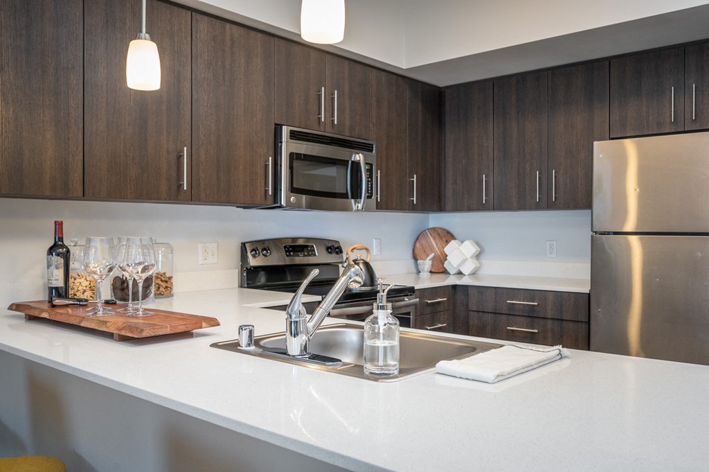 Dog-Friendly Apartments in Everett WA - The Waterline - Kitchen with Stainless Steel Appliances, Quartz Countertops, Dark Wood-Style Cabinetry, Pendant Lighting, Breakfast Bar, and Vinyl Hardwood Floo
