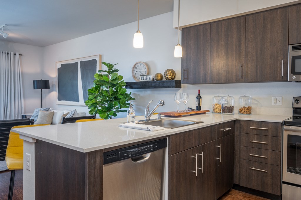 Dog-Friendly Apartments in Everett WA - The Waterline - Kitchen with Stainless Steel Appliances, Quartz Countertops, Dark Wood-Style Cabinetry, Pendant Lighting, Breakfast Bar, and Vinyl Hardwood Floo