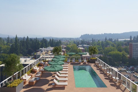 A pool area with sun loungers and umbrellas overlooking a cityscape.