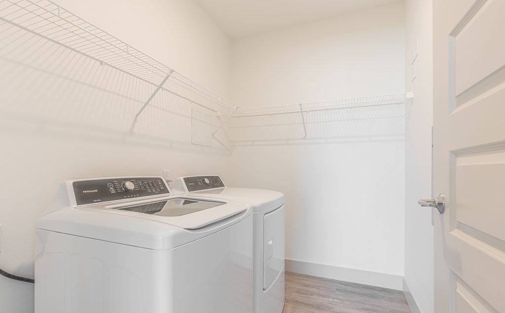 A white washing machine sits in a small, white-walled laundry room.