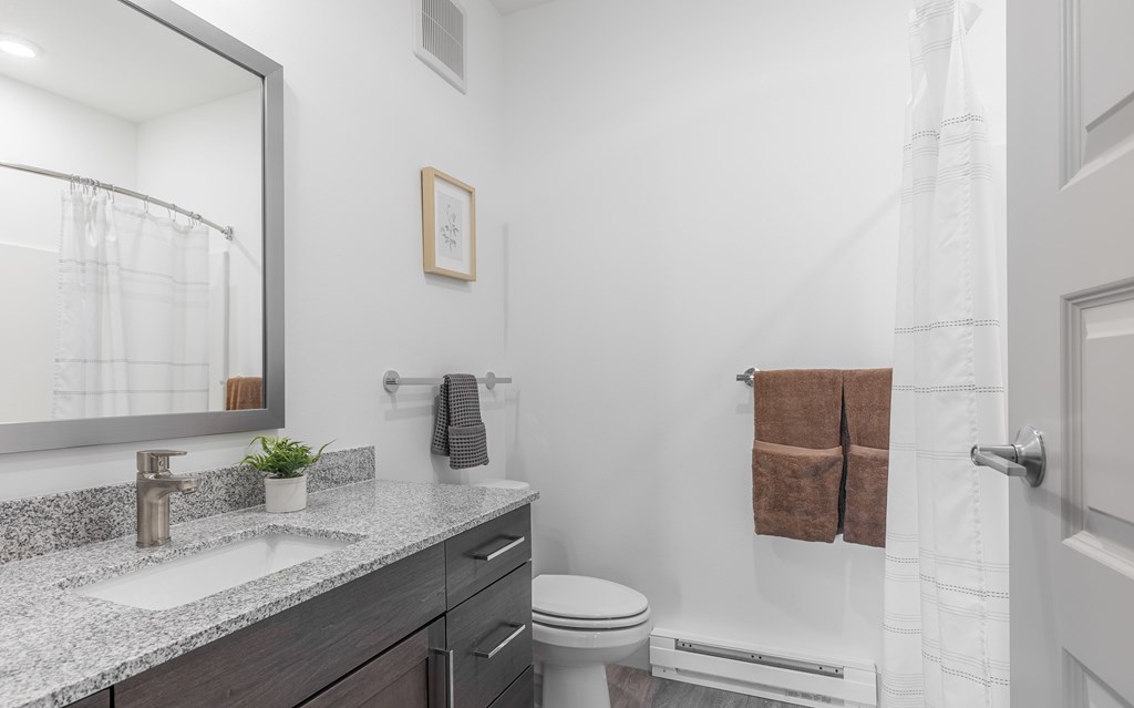 A bathroom with a white toilet, a sink with a mirror above it, and a towel rack with two brown towels.