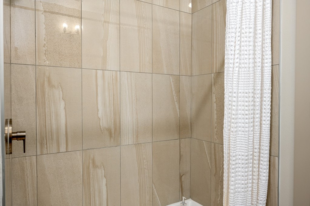 A bathroom with a beige tiled wall and a white shower curtain.
