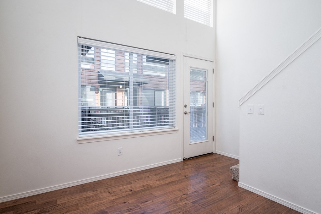 an empty living room with a large window and a door to a hallway