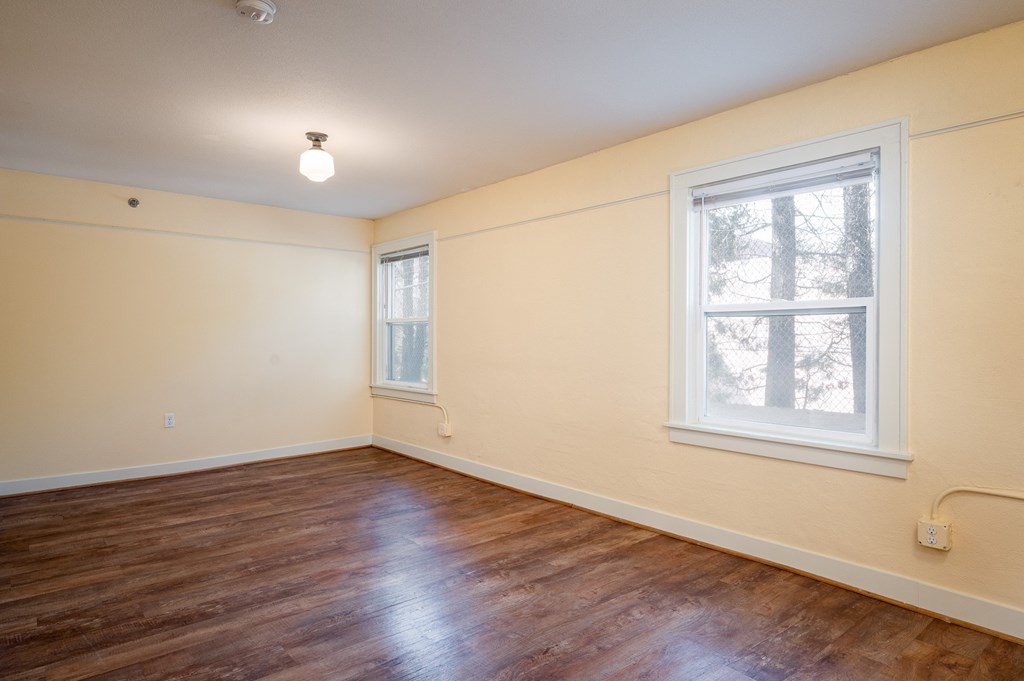 a bedroom with hardwood floors and two windows
