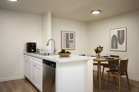 A kitchen with a white countertop and a dining table with chairs.