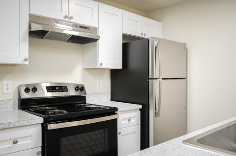A black stove and refrigerator in a kitchen with white cabinets.