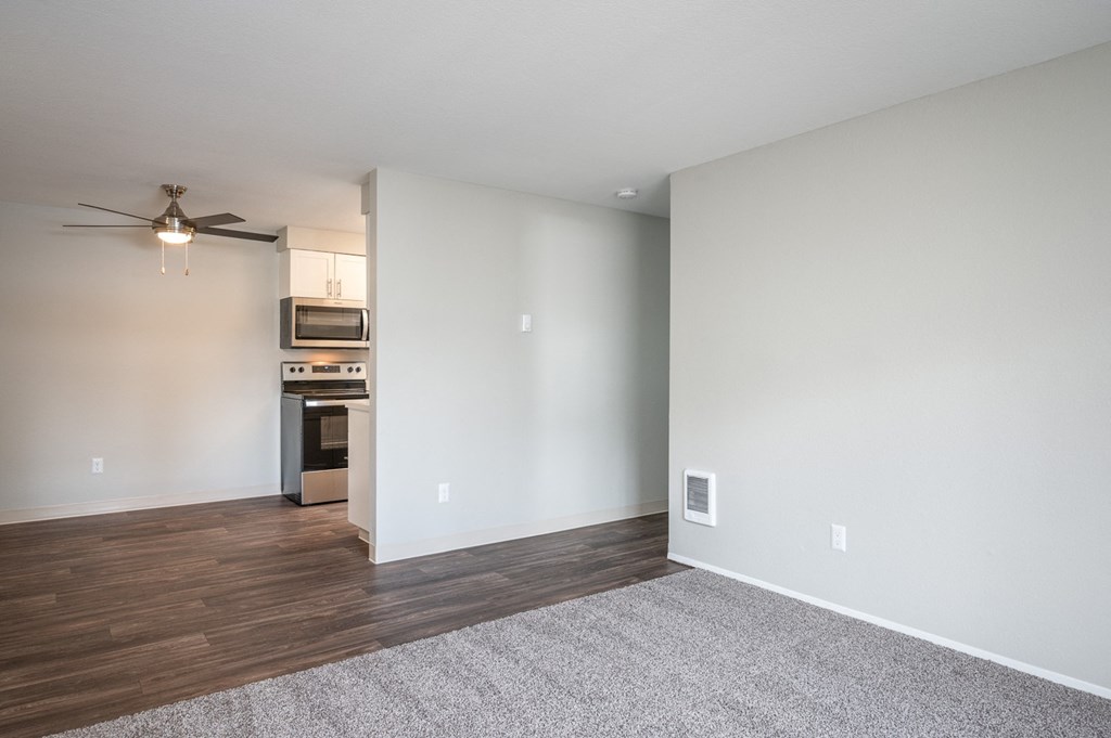 an empty living room with a ceiling fan and a kitchen