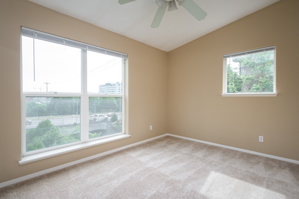 an empty bedroom with two large windows and a ceiling fan