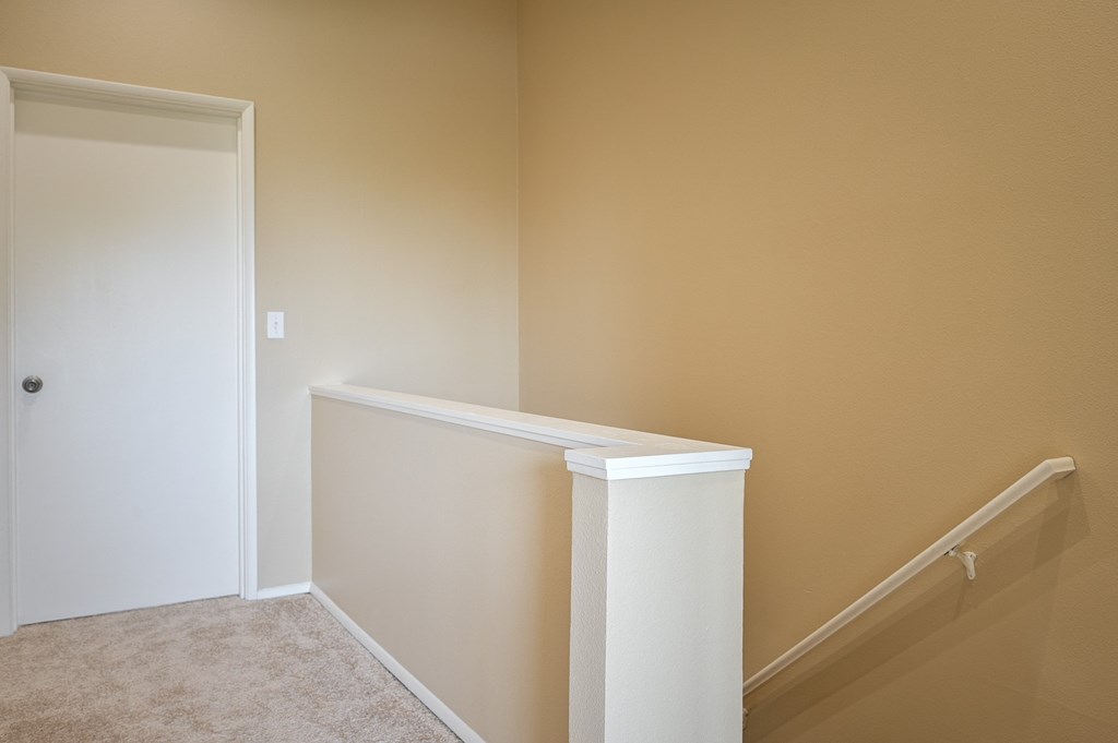 an empty hallway with a staircase and a door to a room with beige walls