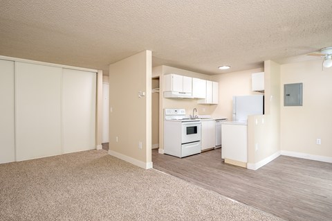 A kitchen with white appliances and cabinets is in a room with a carpeted floor.
